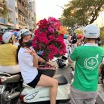 Woman with big pot so flowers on the back of her motorbike
